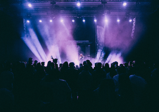 Female artist performing on stage in front of many people, with purple tage lights.