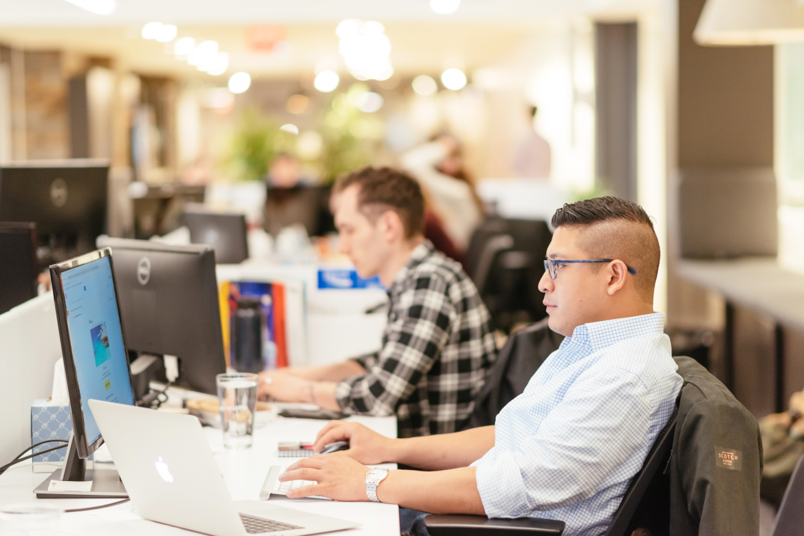 Two men working at desks with laptops and monitors in a modern office.