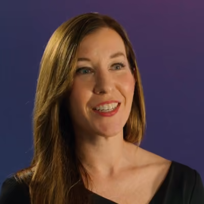 Smiling woman with long brown hair wearing an off-shoulder black top against a purple background.