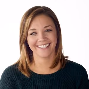 Smiling woman with shoulder-length light brown hair wearing a dark green sweater against a white background.