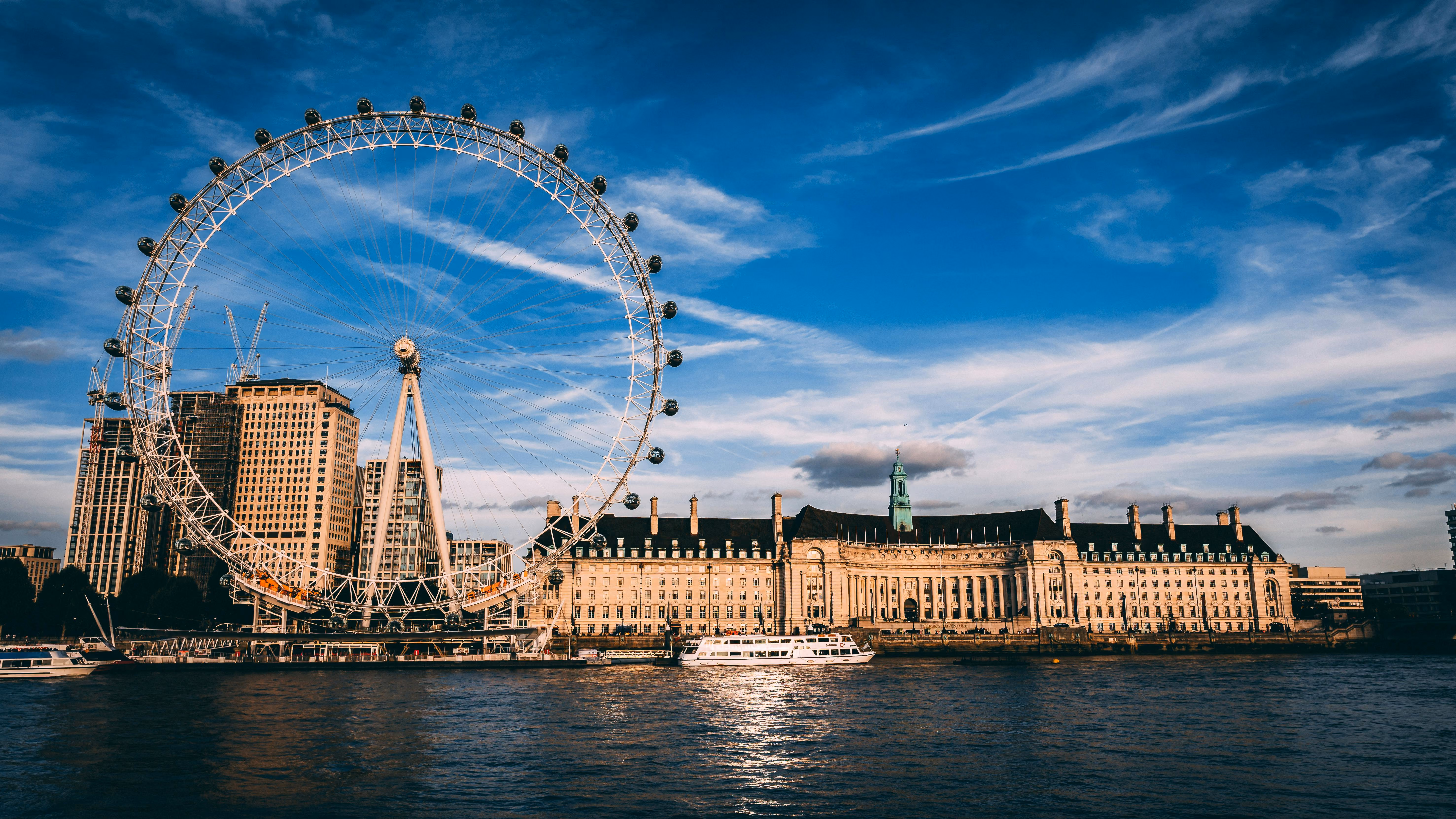 The London Eye Ferris wheel and historic buildings along the River Thames under a blue sky with wispy clouds.