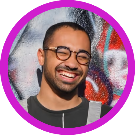 Smiling man with glasses standing in front of a colorful graffiti wall.