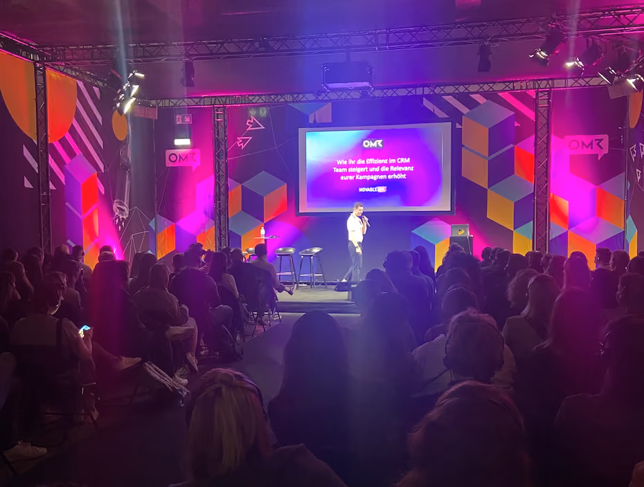 Speaker presenting on stage to a seated audience with a large screen displaying a CRM efficiency topic at the OMR event.