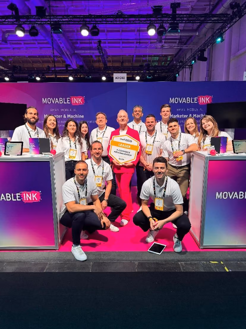 Group of twelve people at a Movable Ink booth, with one person in red holding a Leader badge for e-commerce personalization.