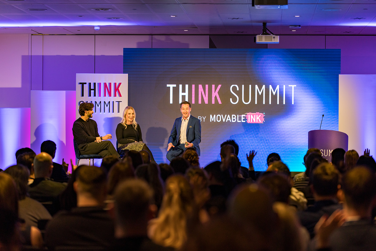 Three panelists seated on a stage speaking at the THINK Summit by Movable Ink with an audience in the foreground.