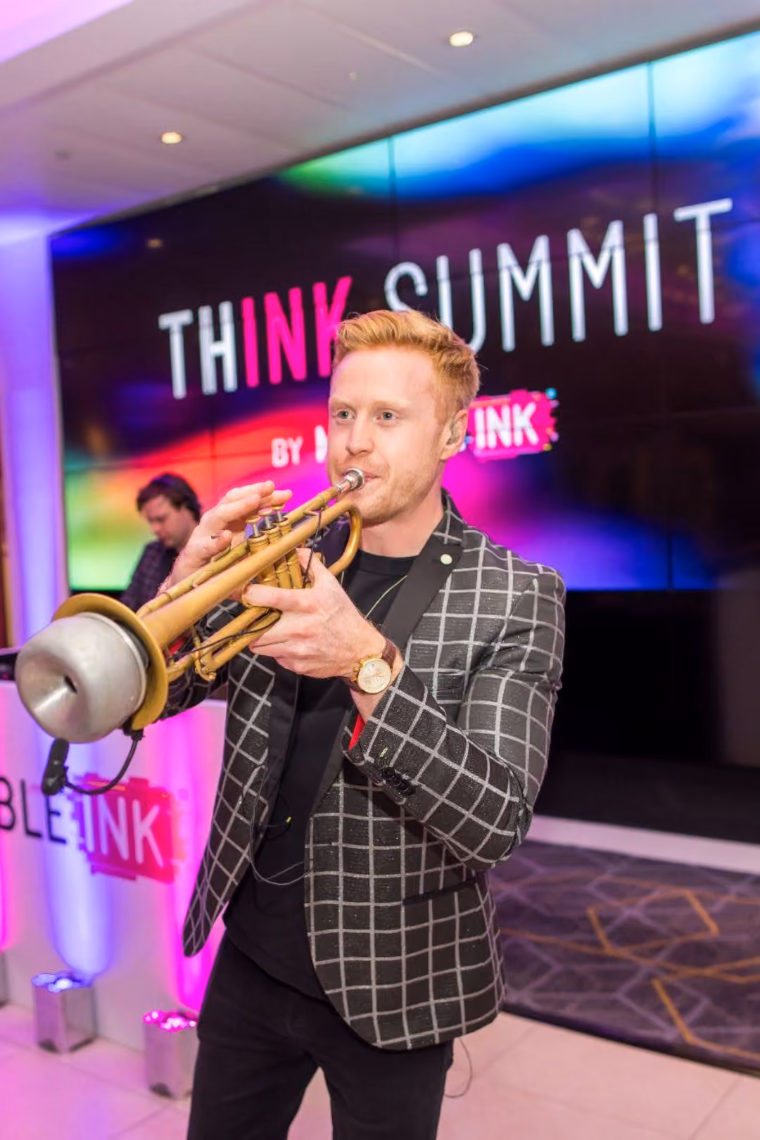 Man in checkered blazer playing a trumpet at the THINK SUMMIT event.
