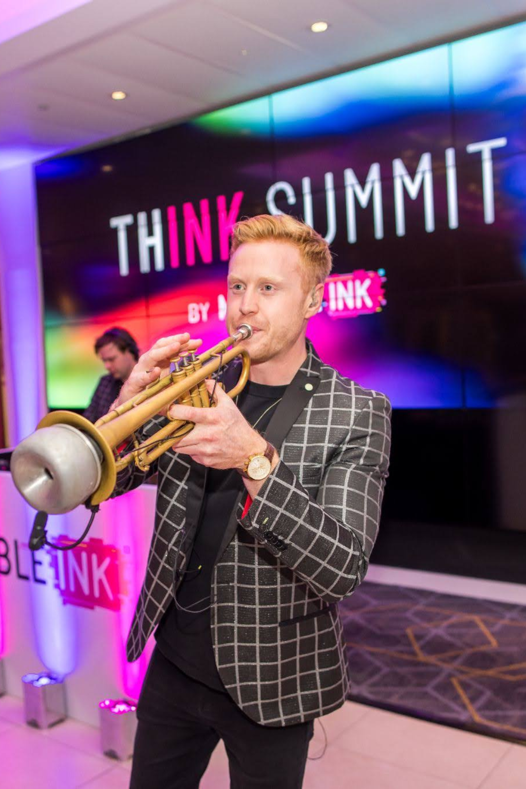 Man in checkered blazer playing a trumpet at the THINK SUMMIT event.