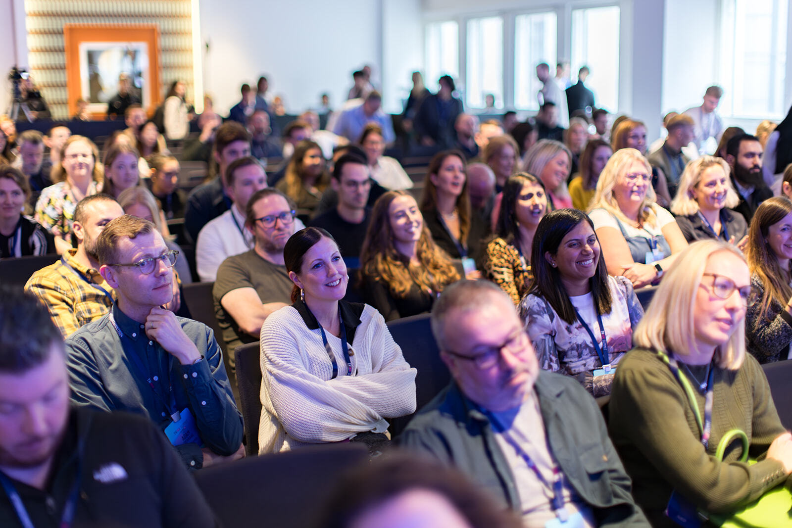 Audience of diverse adults attentively listening and smiling during a conference or seminar in a bright room.