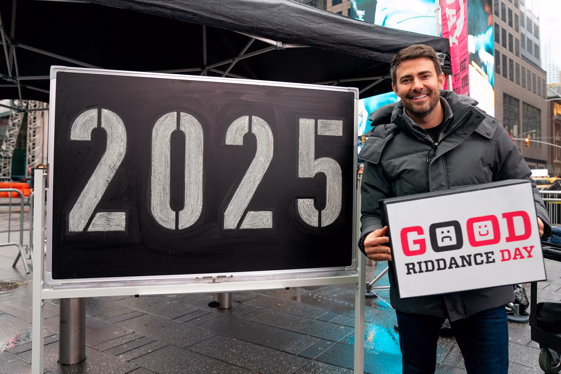 Jonathan Bennett standing in Times Square next to a blackboard reading '2025' with an eraser reading 'Good Riddance Day'
