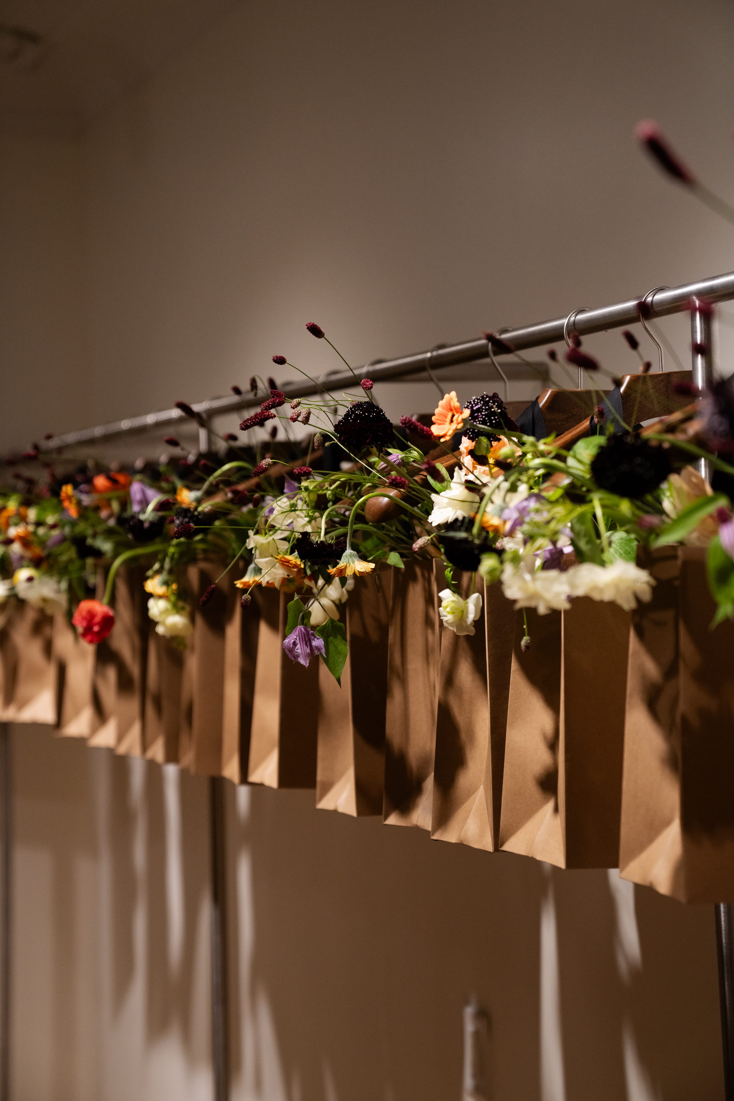 Row of LESET kraft gift bags with floral arrangements hanging along a rail at a LESET brand event