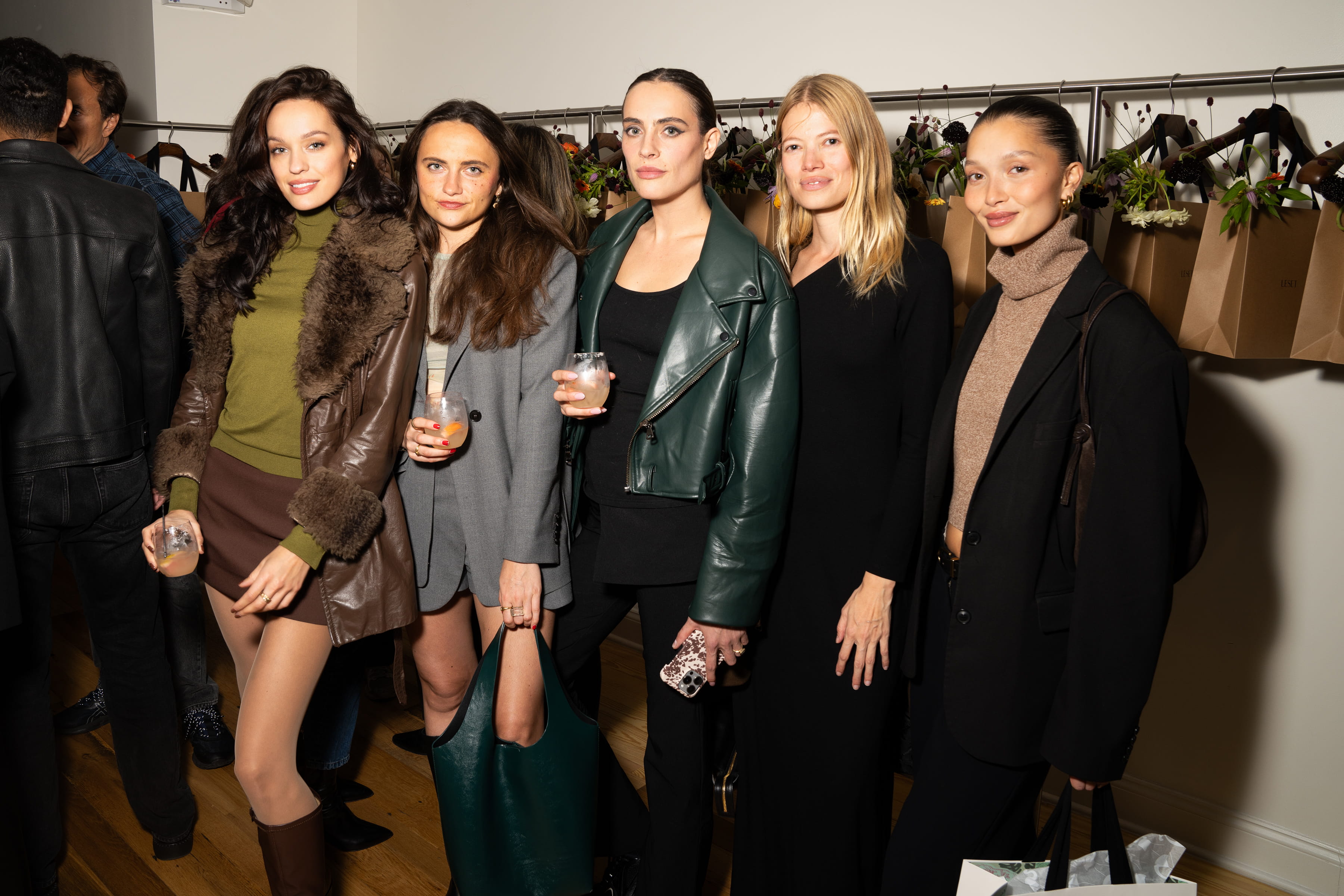 Group of guests holding drinks and mingling at a LESET brand event, with a wall of gift bags and florals in the background