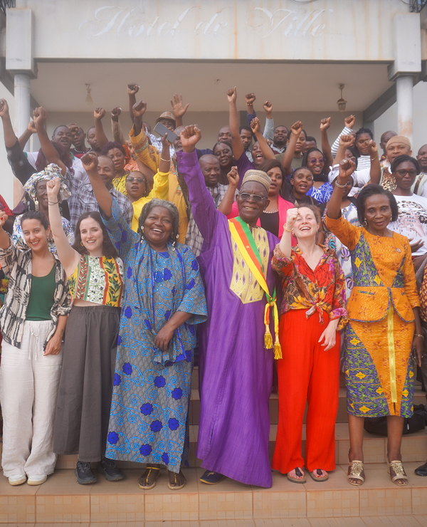 A large, diverse group of smiling people standing on steps, many raising their right fists in a gesture of solidarity or celebration.
