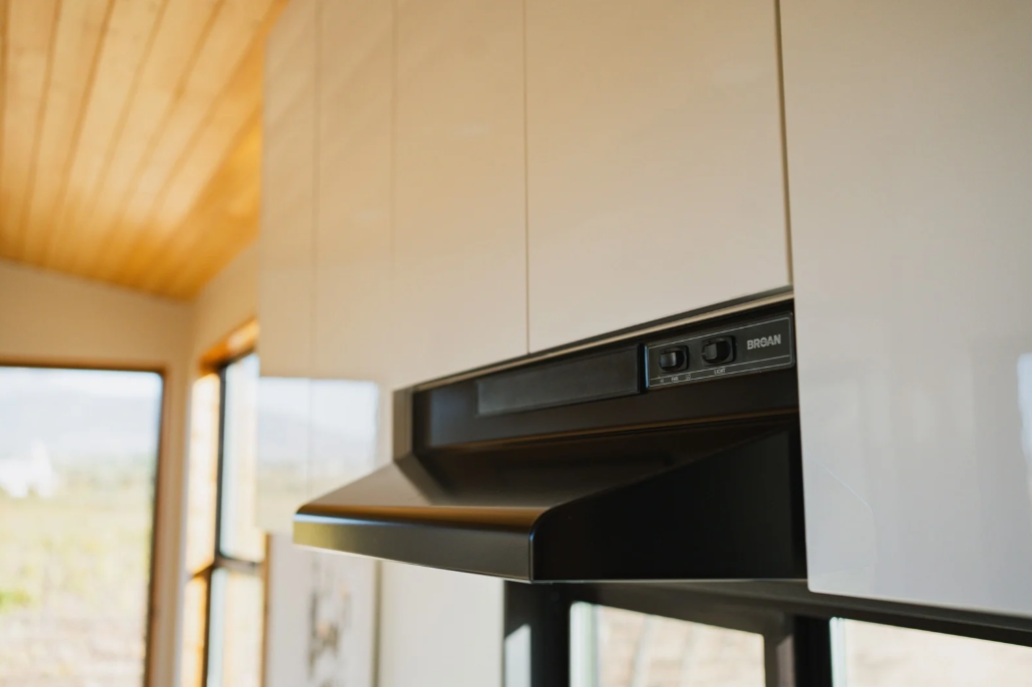 Luxury tiny home kitchen with large quartz countertop and vented range hood.