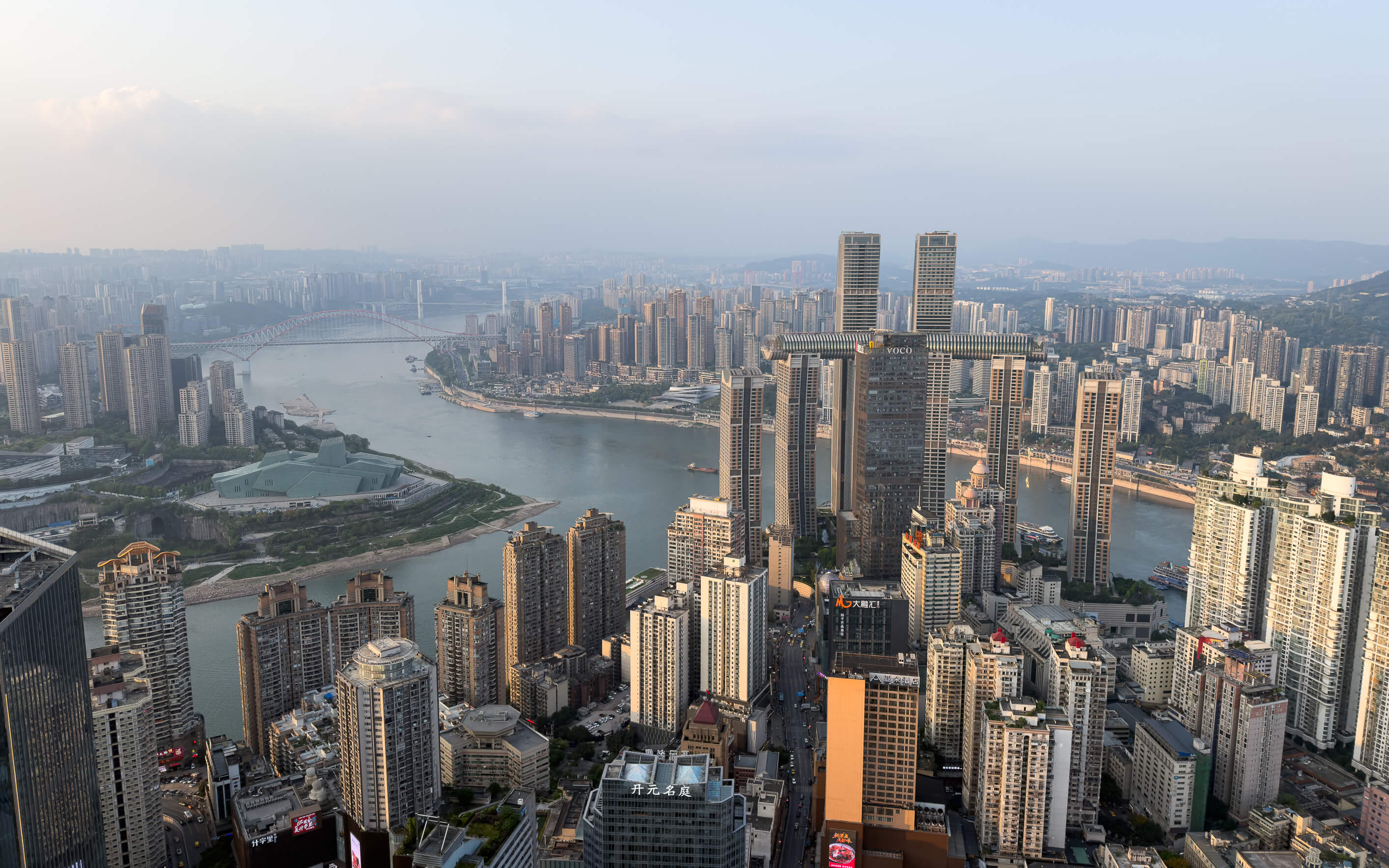Luftaufnahme der chinesischen Metropole Chongqing mit Blick auf die moderne Skyline, zahlreiche Hochhäuser, den windenden Jangtse-Fluss und die dichte Stadtlandschaft unter klarem Himmel.