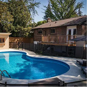 Kidney-shaped inground pool with concrete deck and safety fence
