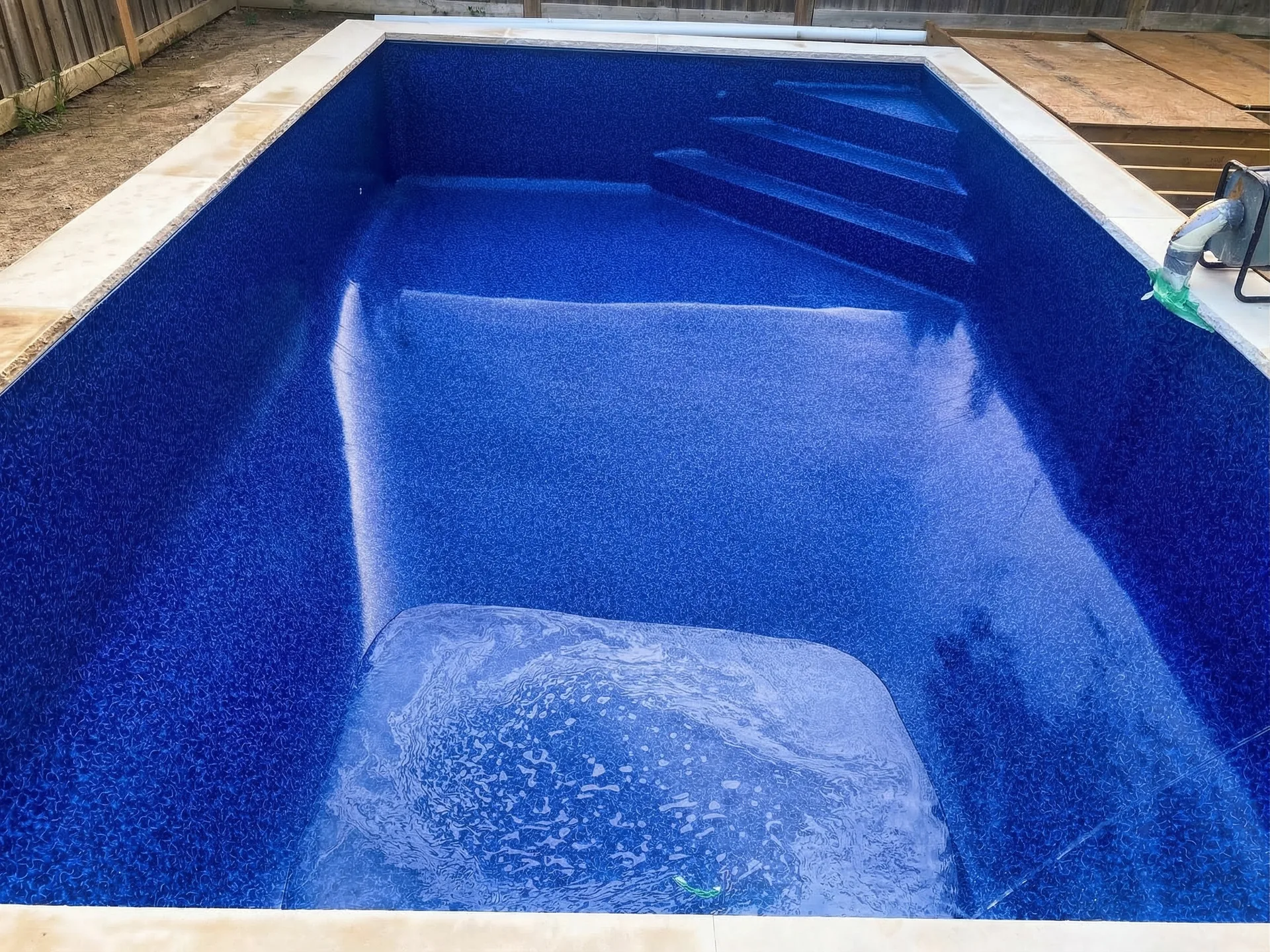Blue vinyl liner freshly installed in 13 by 24 foot pool with tanning ledge in Bradford backyard