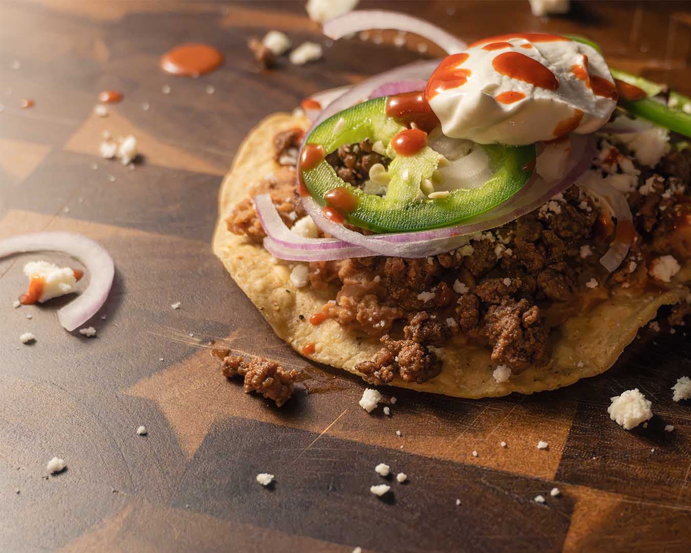 Crispy beef tostada made with Mt. Folly regenerative ground beef, topped with cheese and jalapeños.