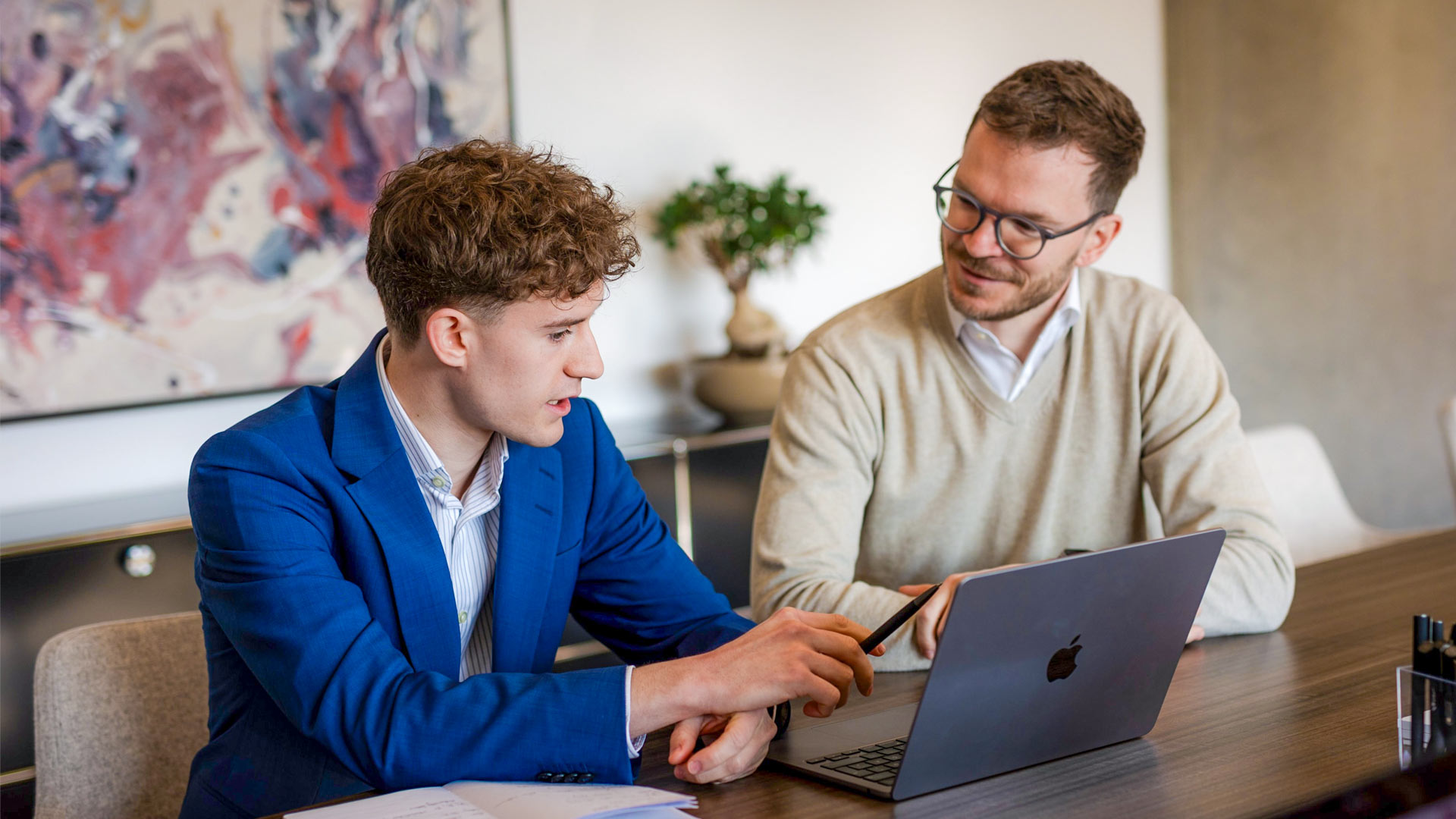 Beratungsgespräch zwischen zwei Kollegen zur steuerlichen Planung eines Immobilienkaufs im Besprechungsraum.