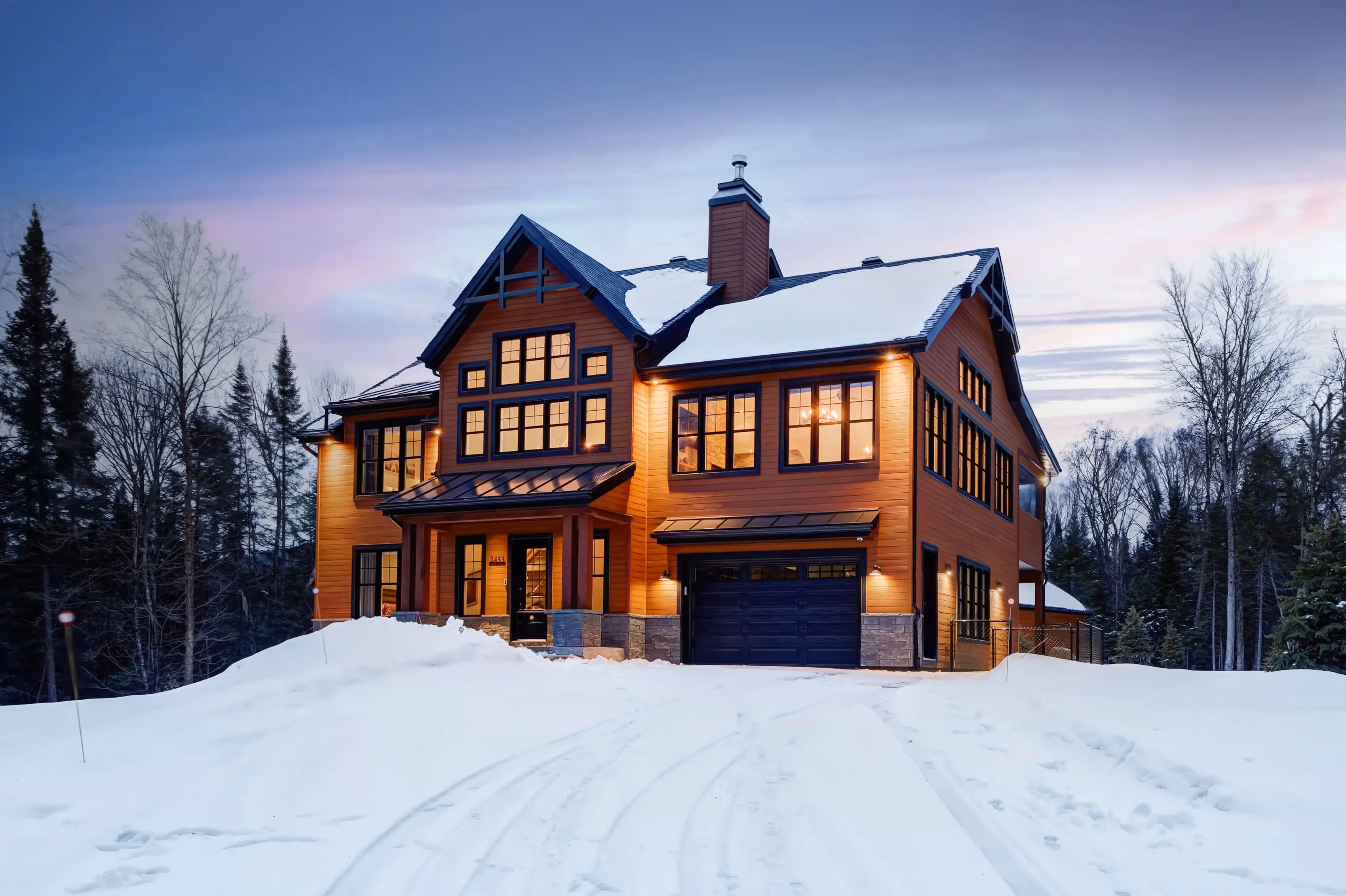 Winter twilight photography by Parsell of a luxury wood chalet covered in snow, showcasing a warm and inviting feel for marketing four-season properties in the Laurentians and Outaouais. | Photographie d'hiver au crépuscule par Parsell d'un chalet de luxe 