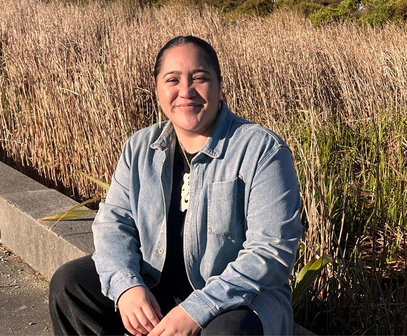 Social and Digital Specialist Darelle Teau sitting outside in front of some tall grass.