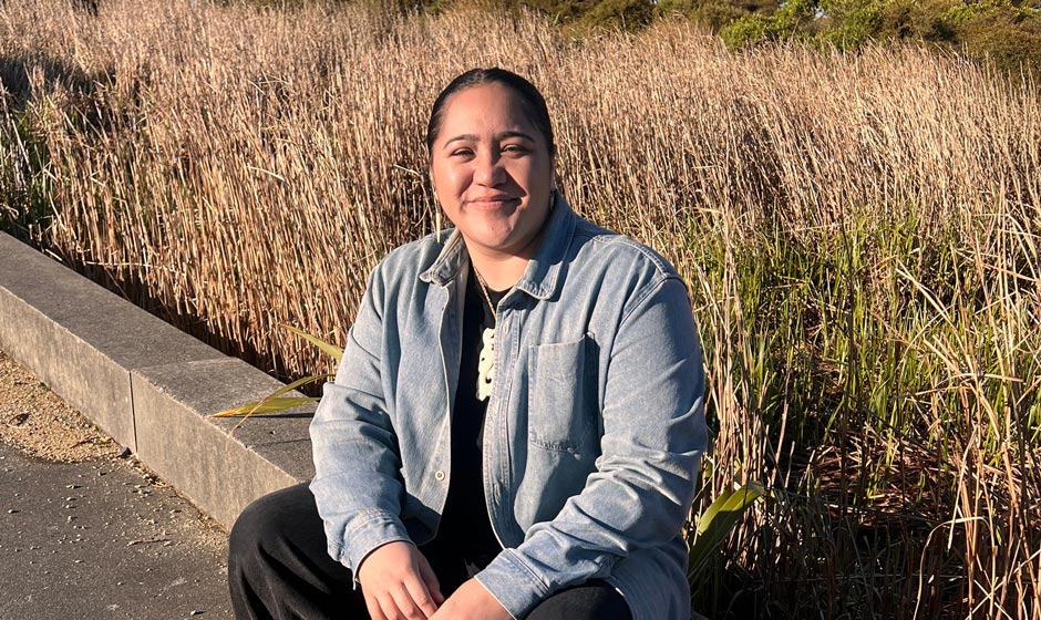 Social and Digital Specialist Darelle Teau sitting outside in front of some tall grass.