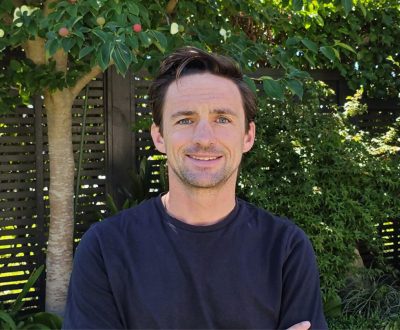 Craig Adolph standing in front of some trees with his arms folded.