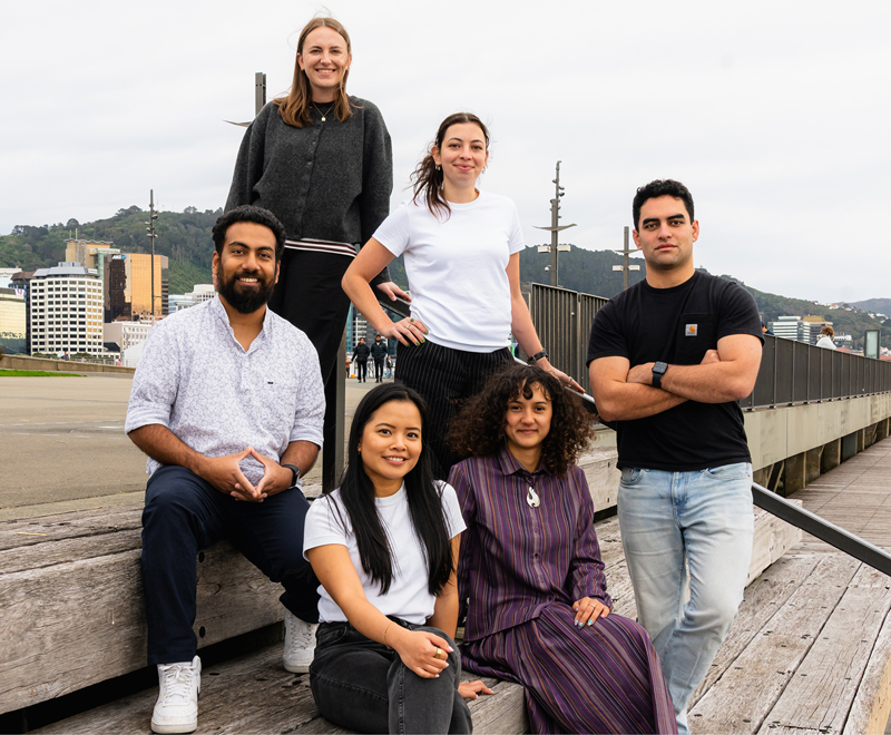 Six people of the Hemisphere team sitting and standing in a hgroup on the Wellington waterfront.