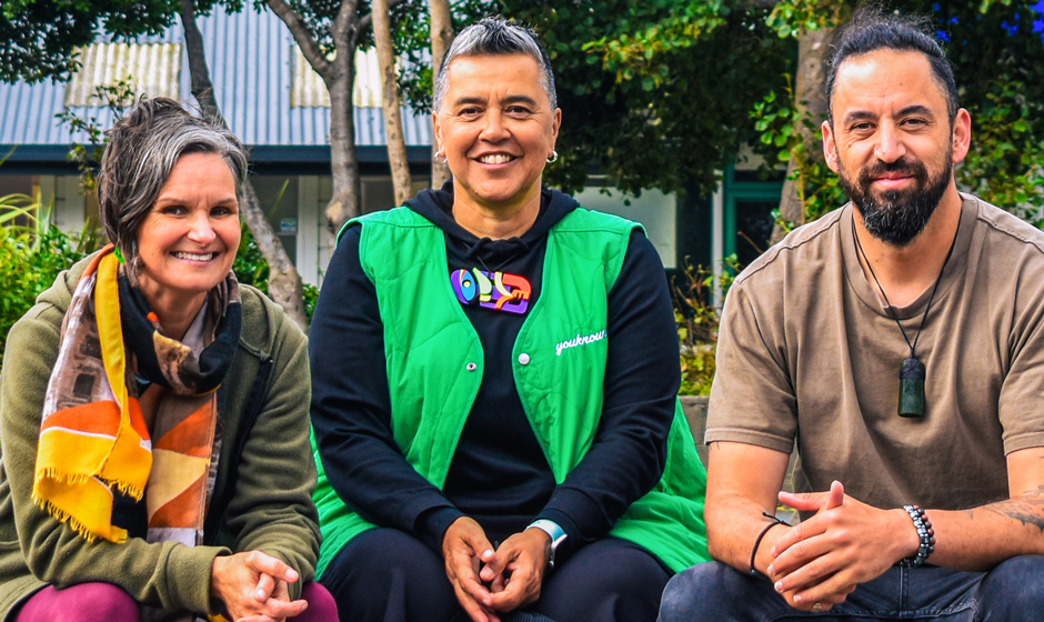 Three smiling basketball coaches sitting on a bench at a basketball court.