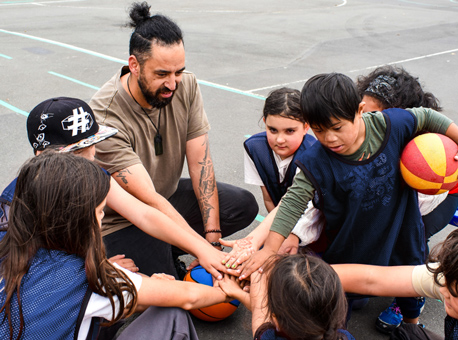A basketball coach sitting on the court with a group of young players.