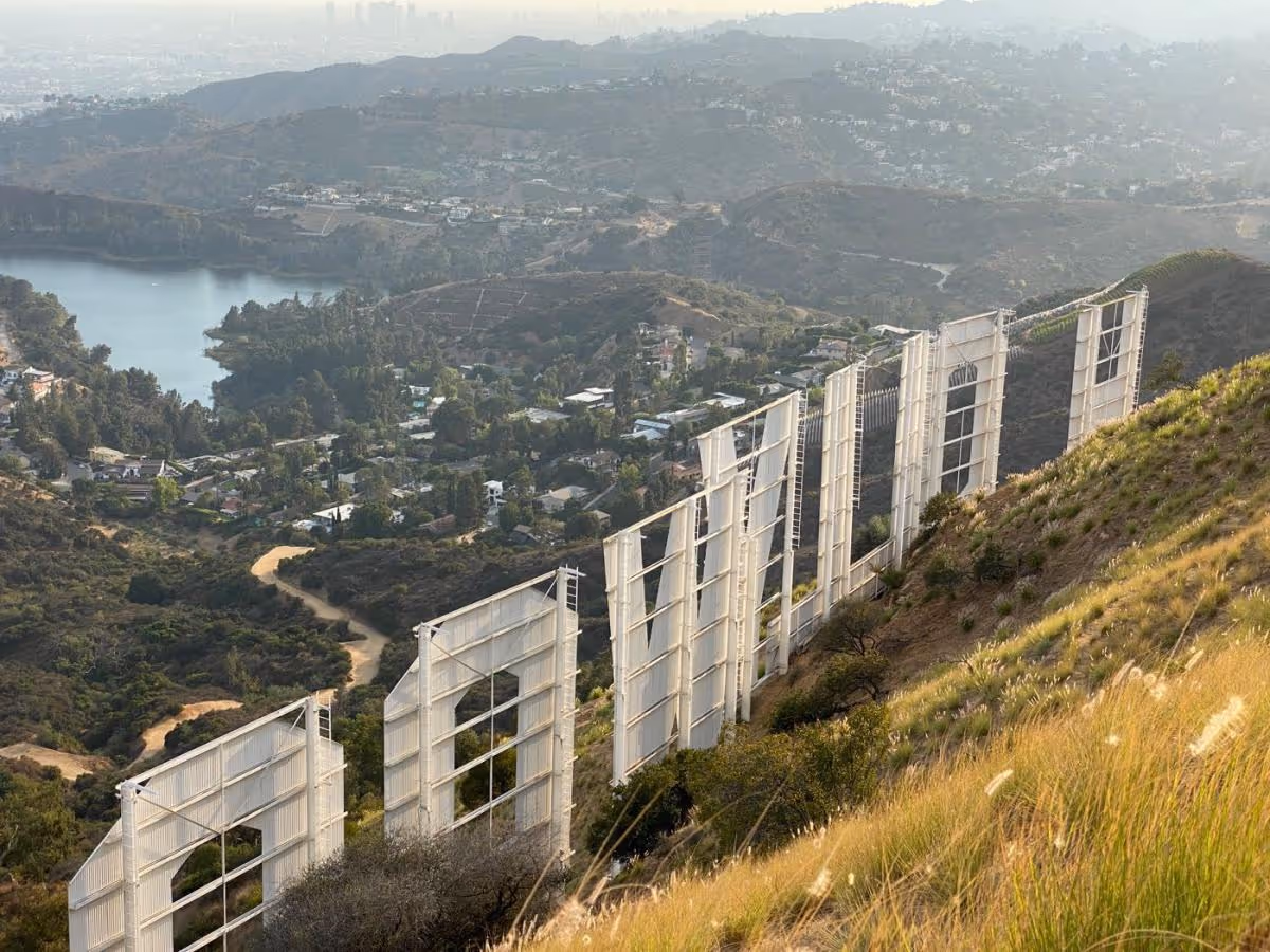 Back view of the Hollywood Sign on a hillside with city and lake in the background.