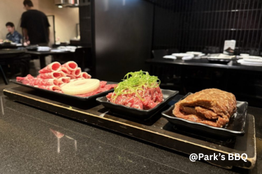 Three platters of sliced raw meats and marinated beef arranged on a counter at Park’s BBQ restaurant.