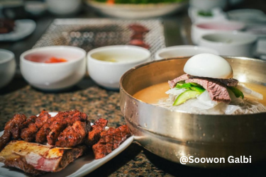 Korean cold noodles topped with sliced beef, cucumber, and half a boiled egg, served beside grilled meat and side dishes at Soowon Galbi.
