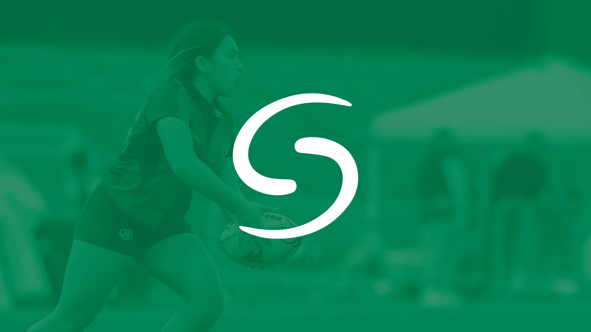 Female rugby player running while holding a rugby ball on a field with blurred spectators in the background.