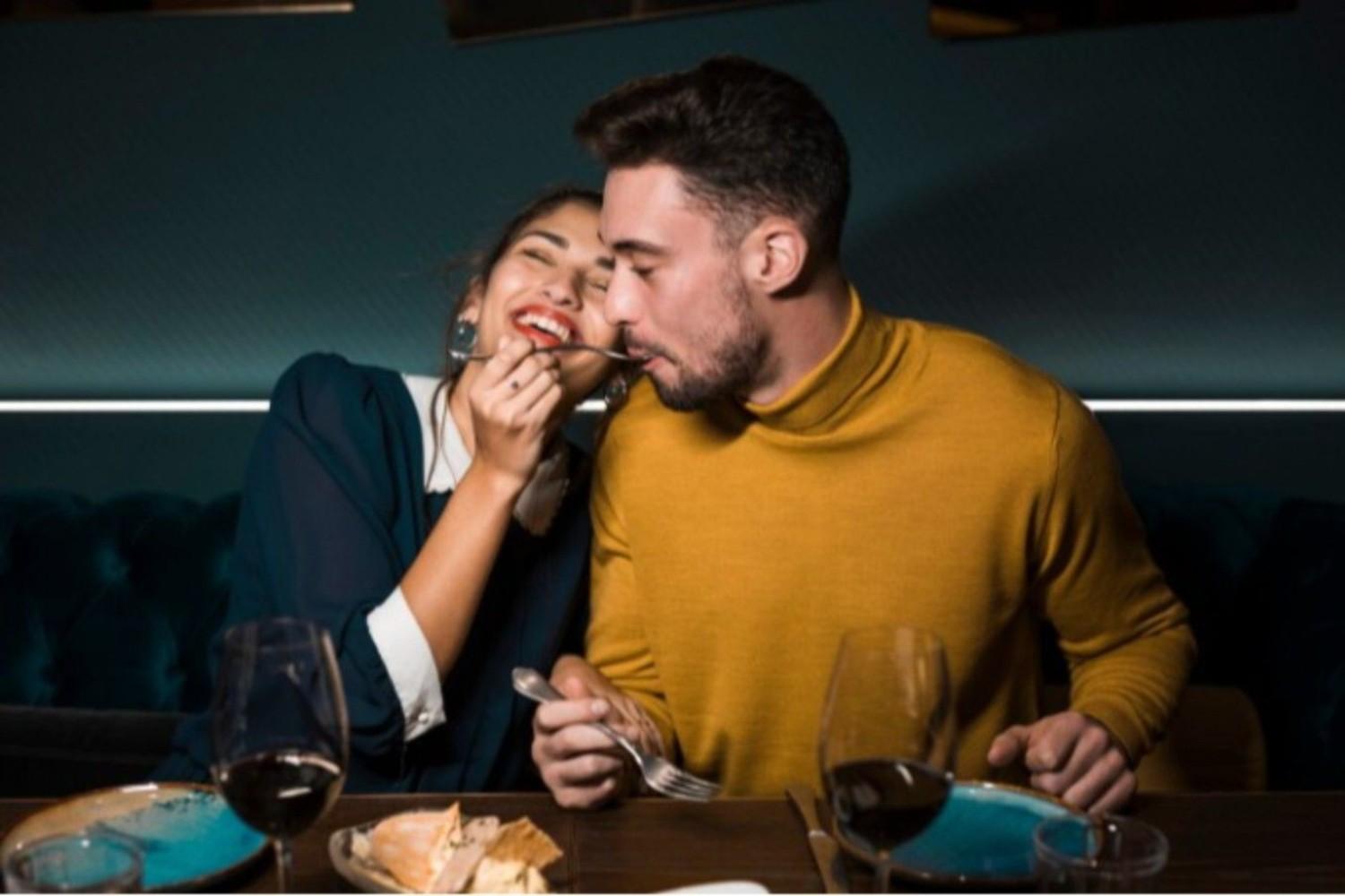 Man with fork in mouth near cheerful woman at table with glasses of wine and food in restaurant