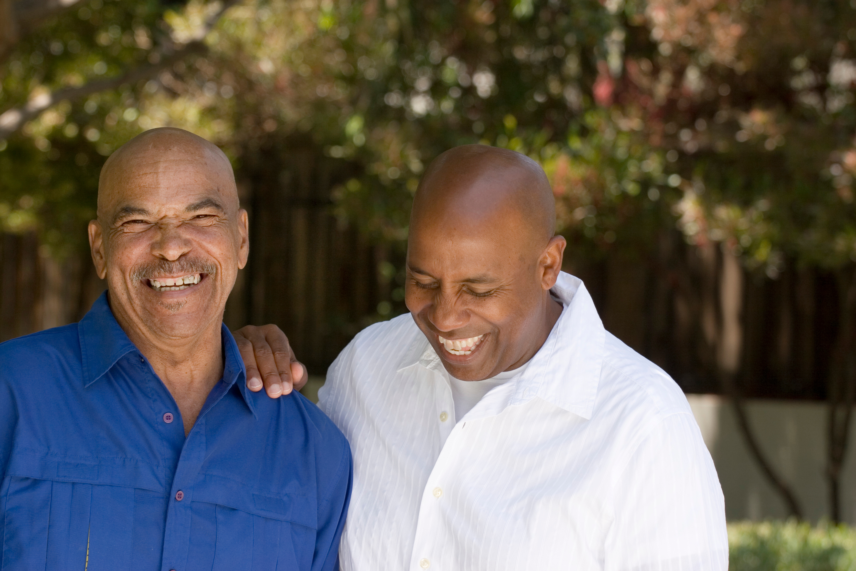 Father and adult son laughing together outdoors, one with an arm around the other's shoulder