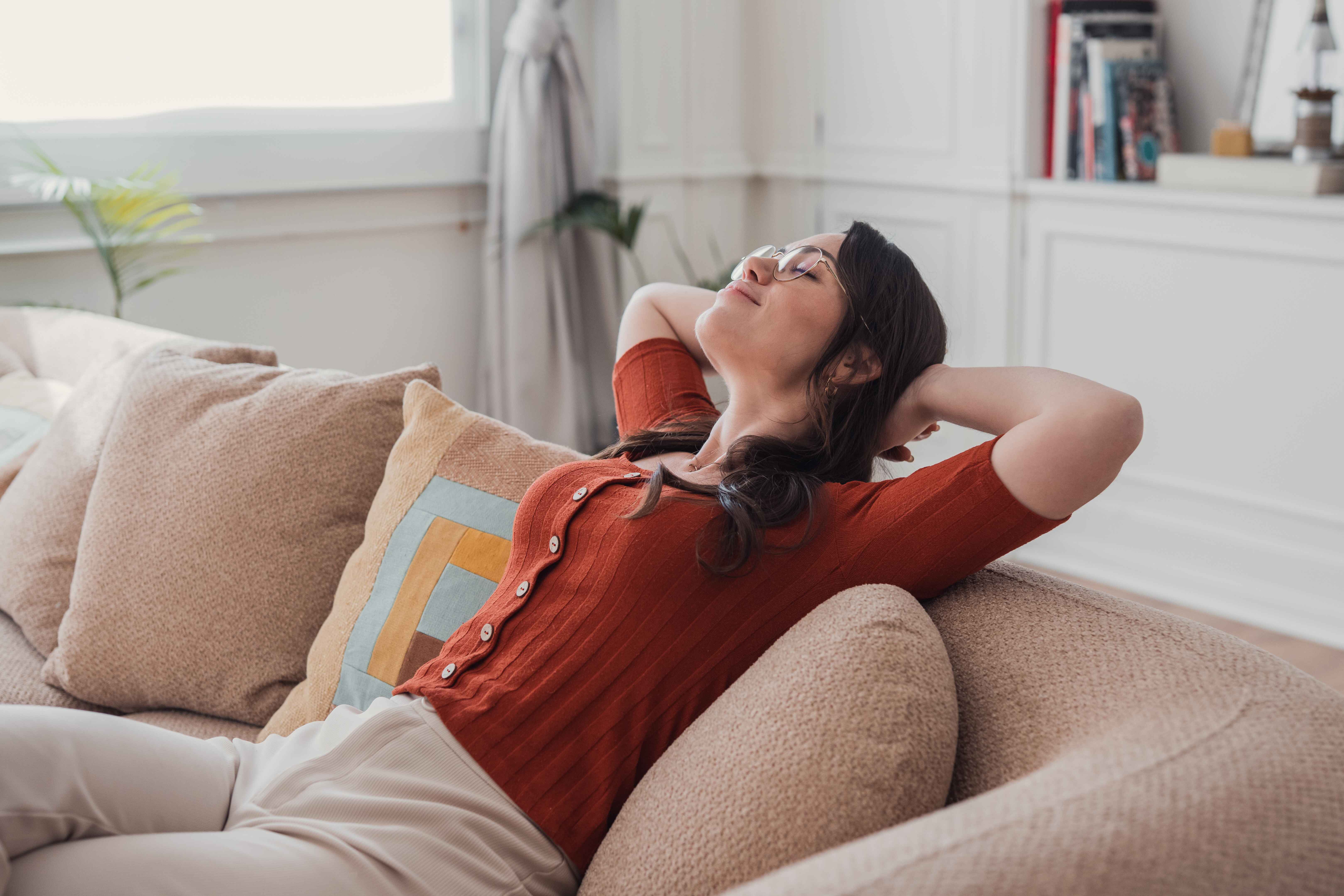 Woman relaxing on a couch with her eyes closed and arms behind her head, looking relieved