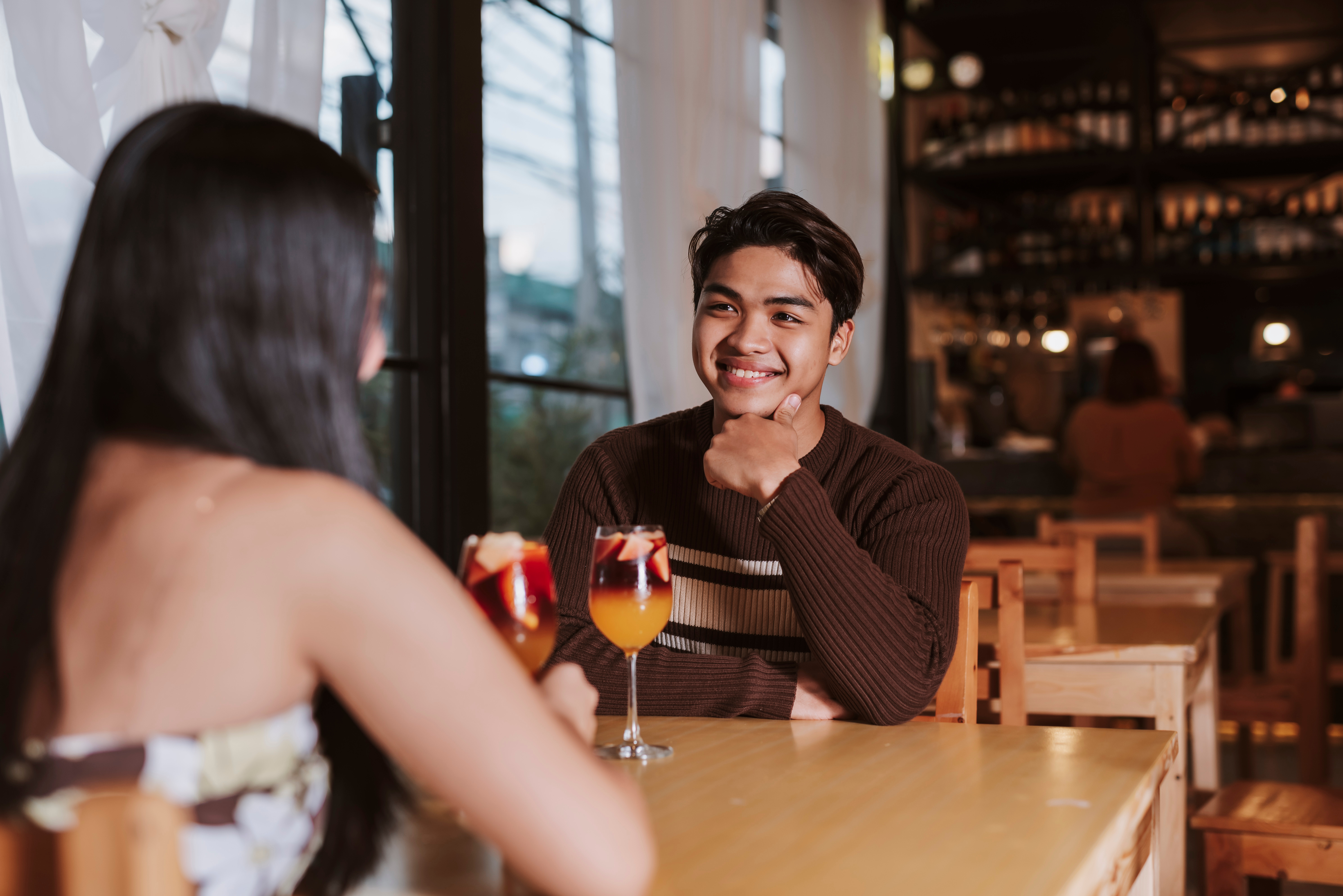 Man leaning forward with his chin on his hand, smiling at a woman across a bar table