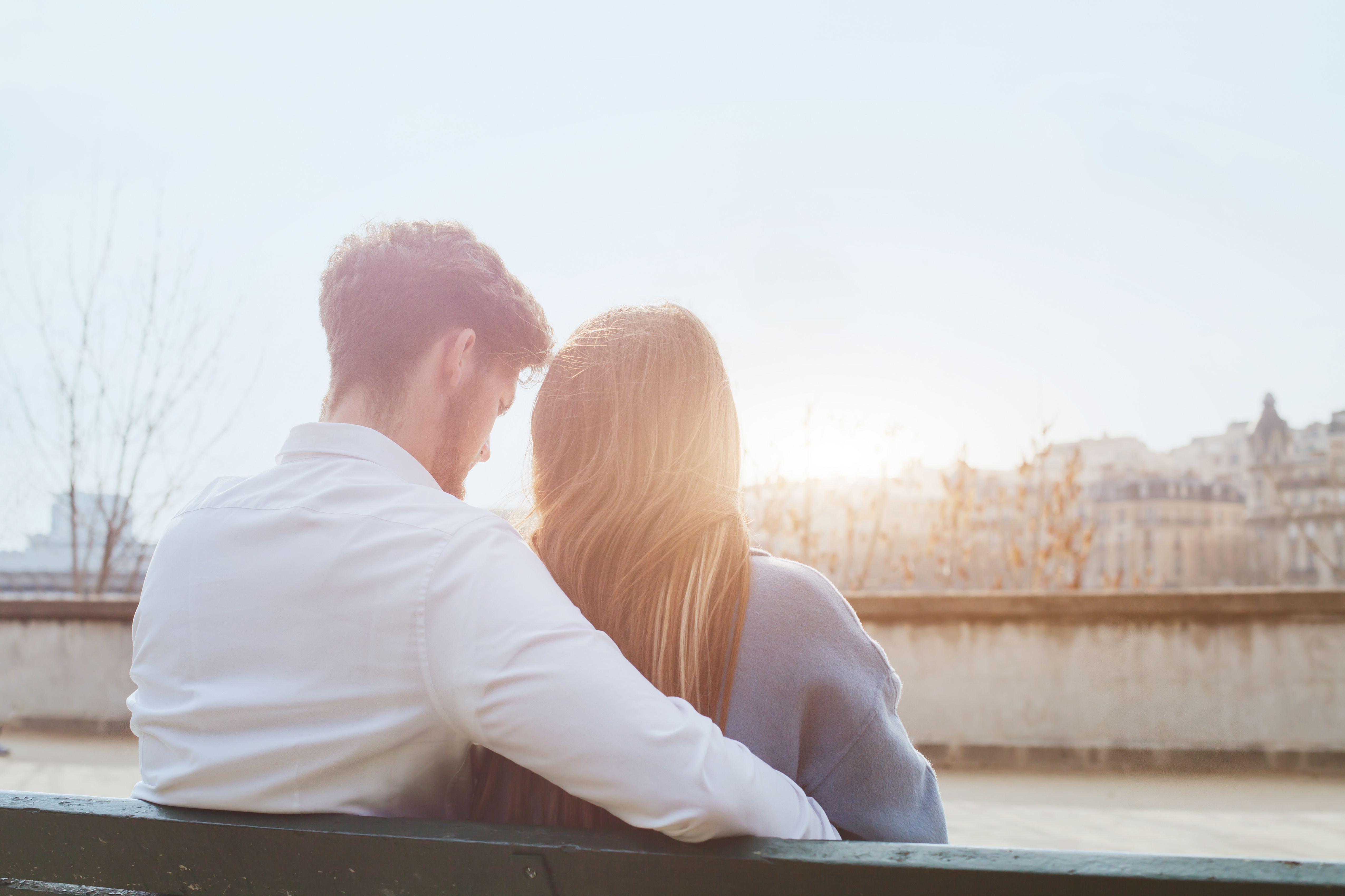 Couple sitting closely on a bench, embracing while looking out over a sunlit city skyline