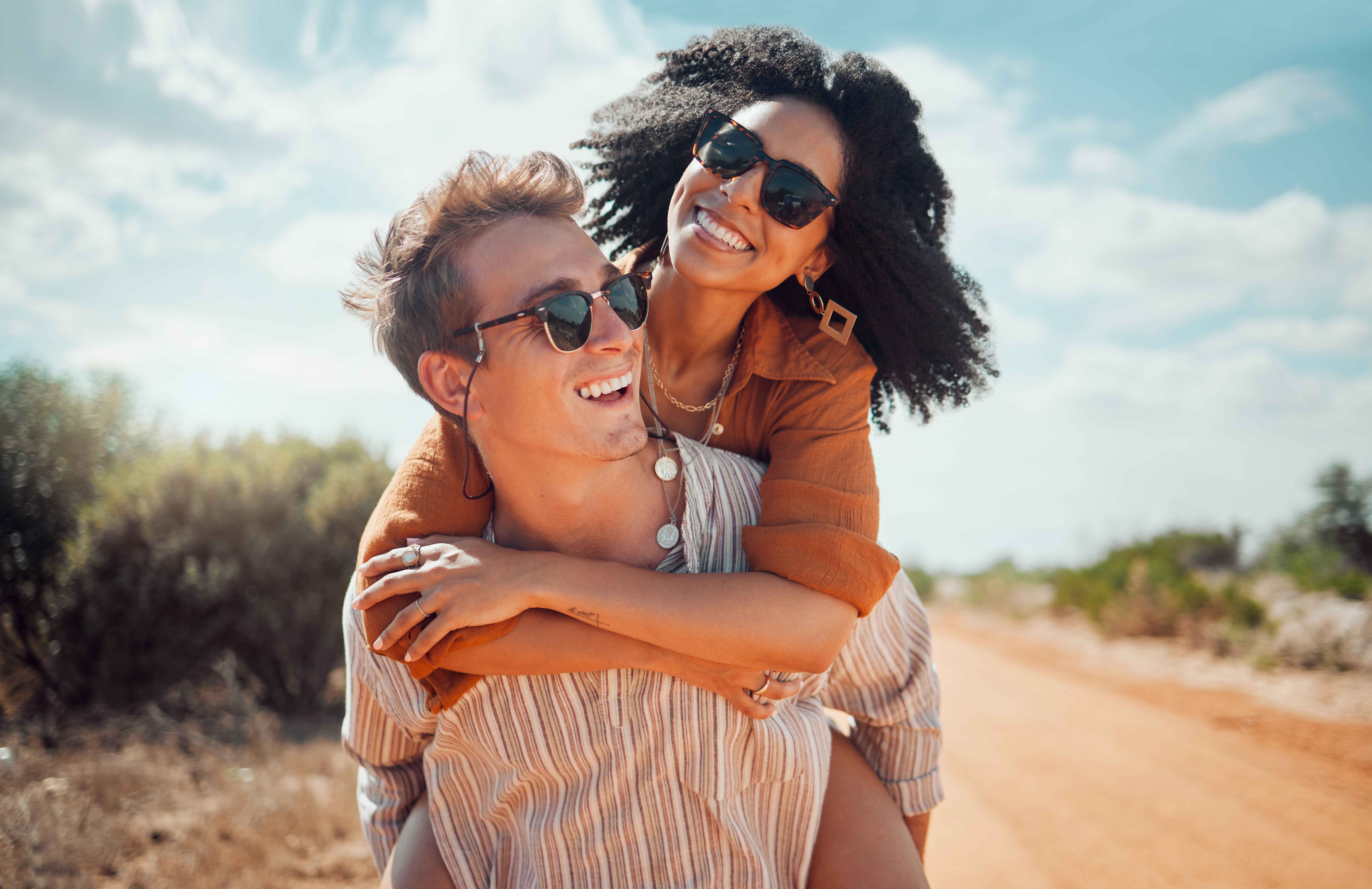 Smiling couple laughing outdoors, woman on partner's back on a sunlit dirt road