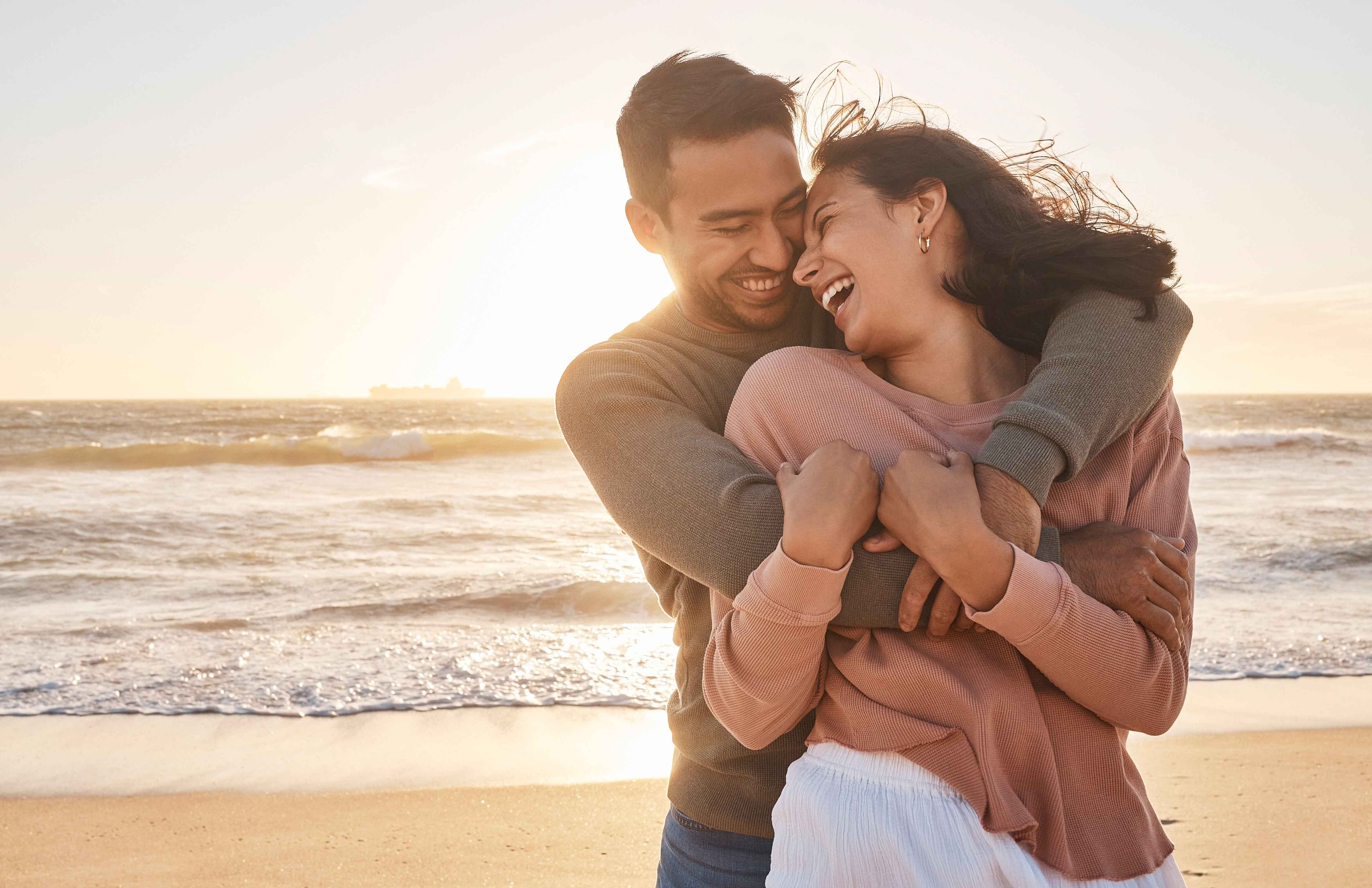 Couple embracing and laughing together on a beach at sunset
