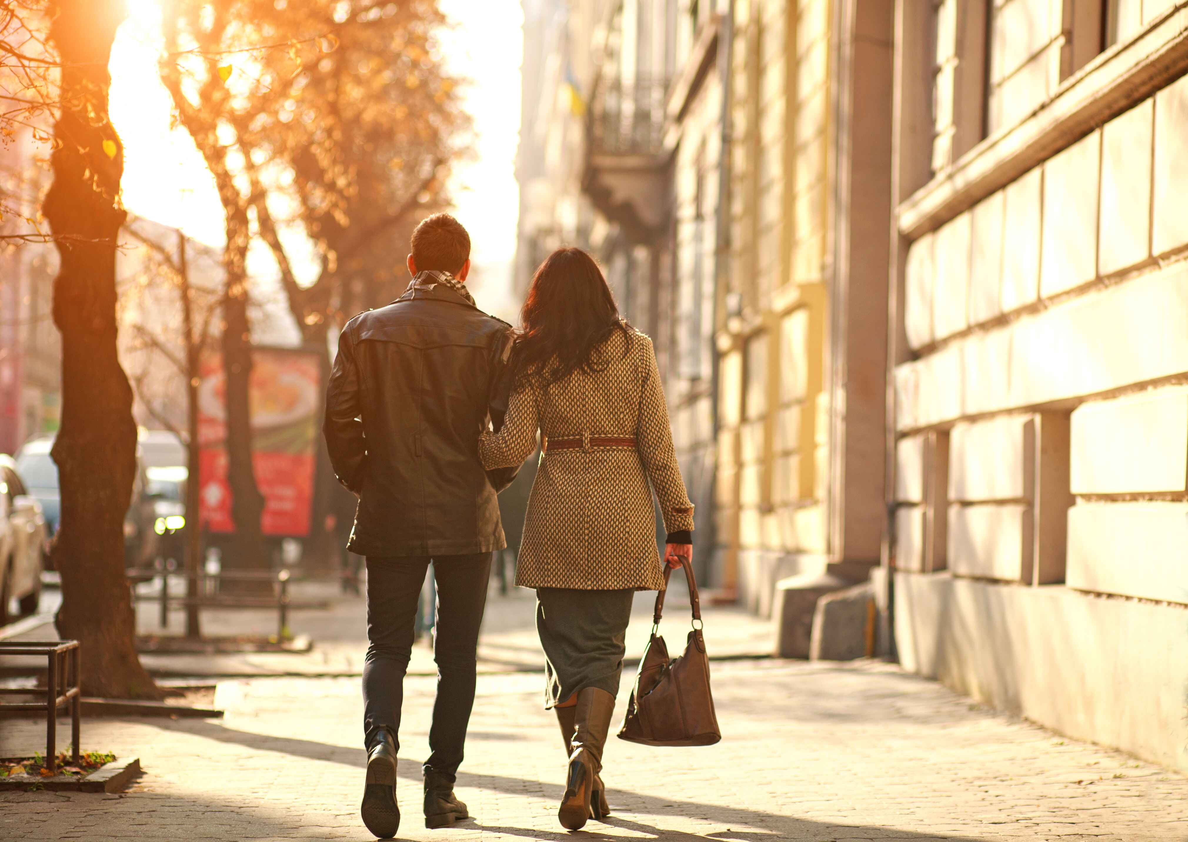 Couple walking arm in arm down a sunlit city street at sunset