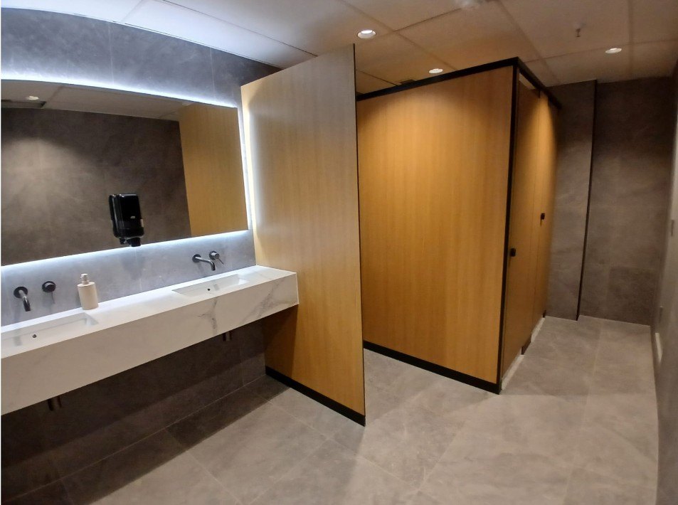 Renovated washroom with stone vanity, backlit mirror and timber cubicle doors