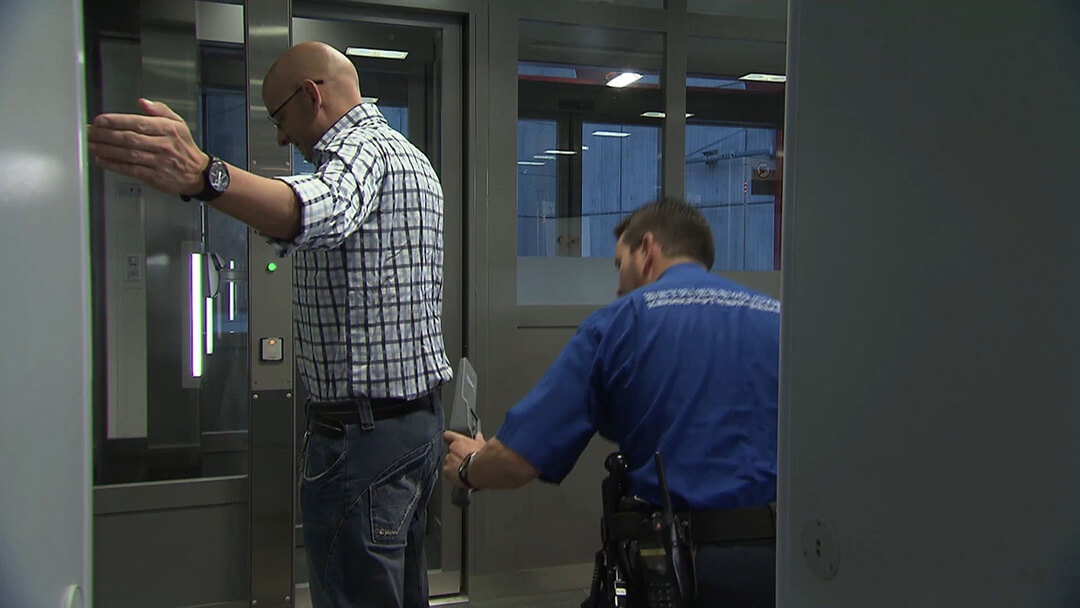 Ein Mann wird von einem Sicherheitsbeamten mit einem Handscanner gescant.