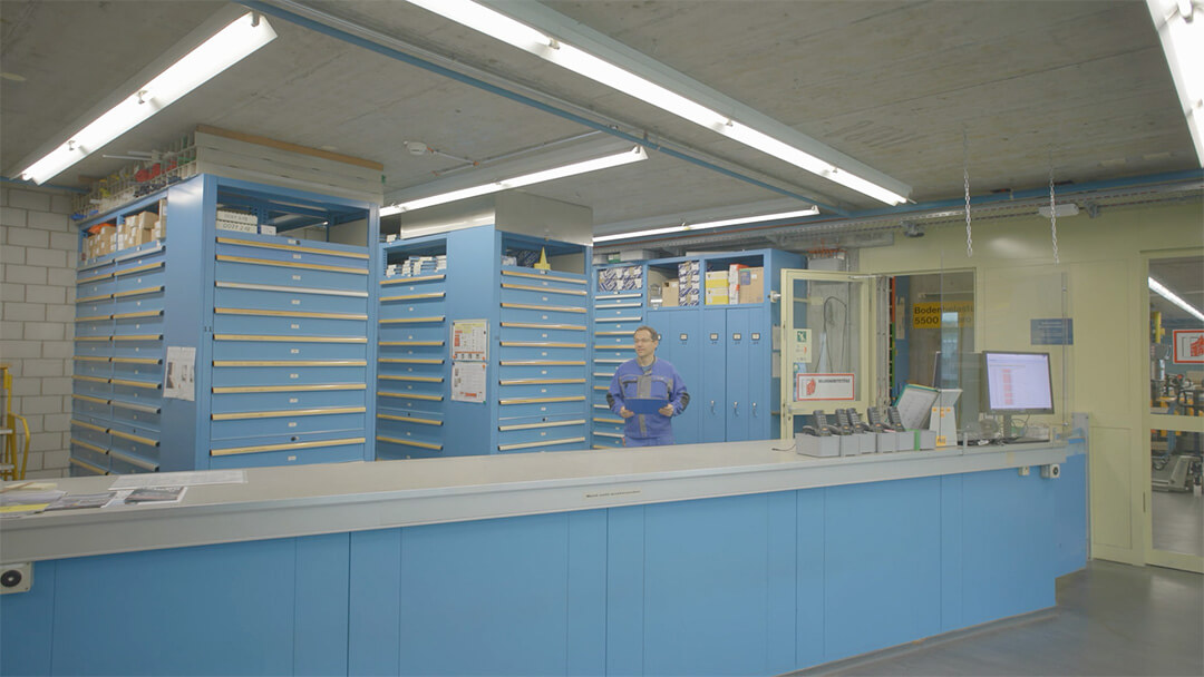 Ein Arbeiter steht in einem ordentlichen Lagerraum mit blauen Schubladenschränken und Theke.