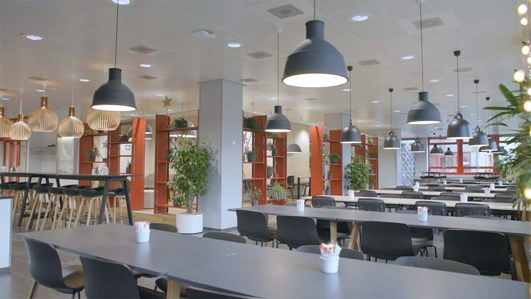 Moderne kantine mit langen tischen, schwarzen stühlen, hängenden lampen und pflanzen.
