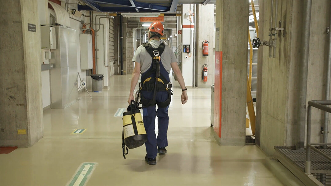Arbeiter mit Helm und Sicherheitsgurt trägt Ausrüstung in einem Industriebereich.