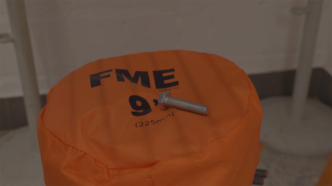 Ein silberner Schraubbolzen liegt auf einem orangefarbenen Polster mit der Aufschrift FME 9" (225 mm²).