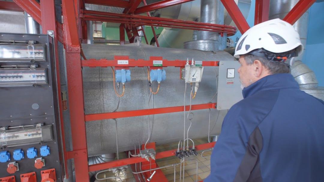 Ein Mann mit Helm und blauer Arbeitsjacke prüft industrielle Steuergeräte und Ventile.