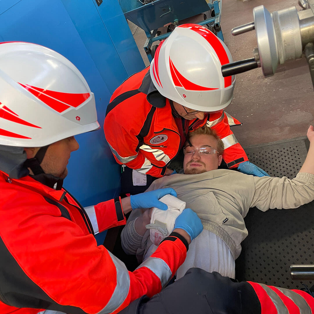 Zwei Sanitäter in Schutzhelmen versorgen eine am Boden liegende Person mit einer Verletzung.