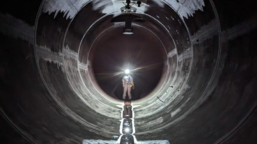 Arbeiter mit Helm und Stirnlampe steht in einem langen dunklen Tunnel mit Wasser auf dem Boden.